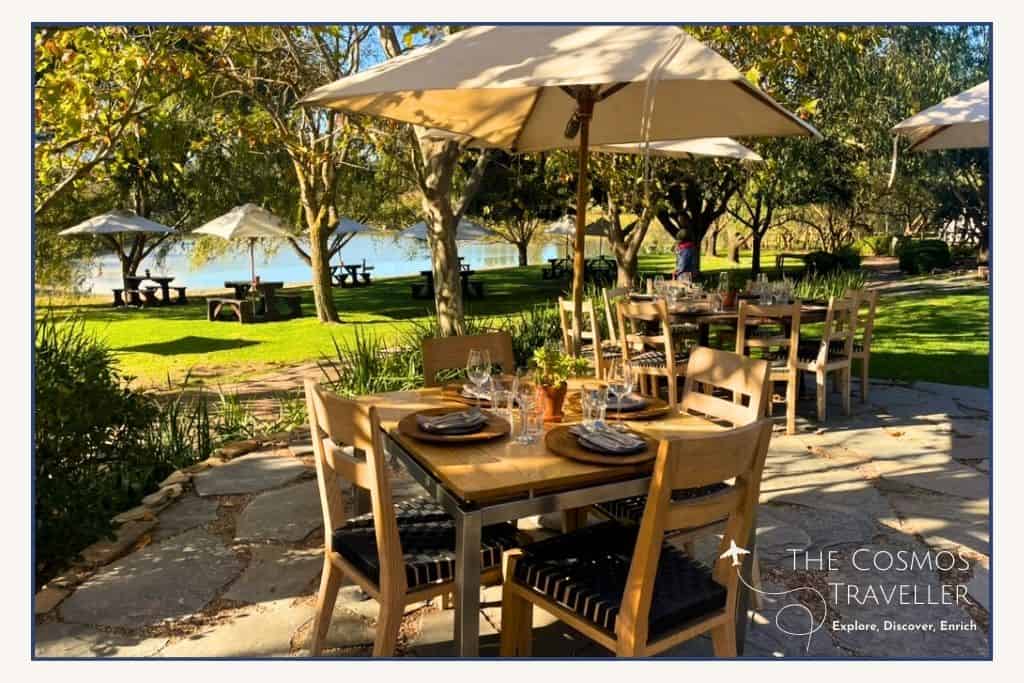 A bright sunny day, a table is laid for lunch with a parasol for shade. 