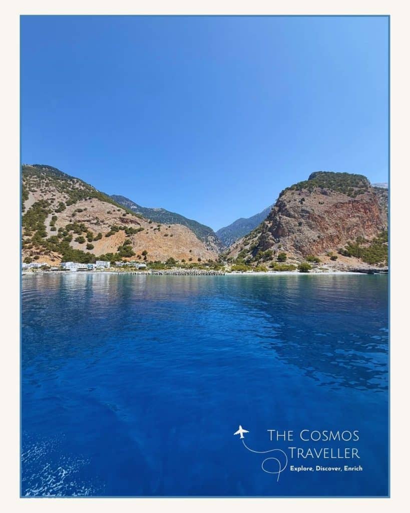 View from boat of deep blue waters off southern Crete, with Agia Roumeli and Samaria Gorge in the distance.