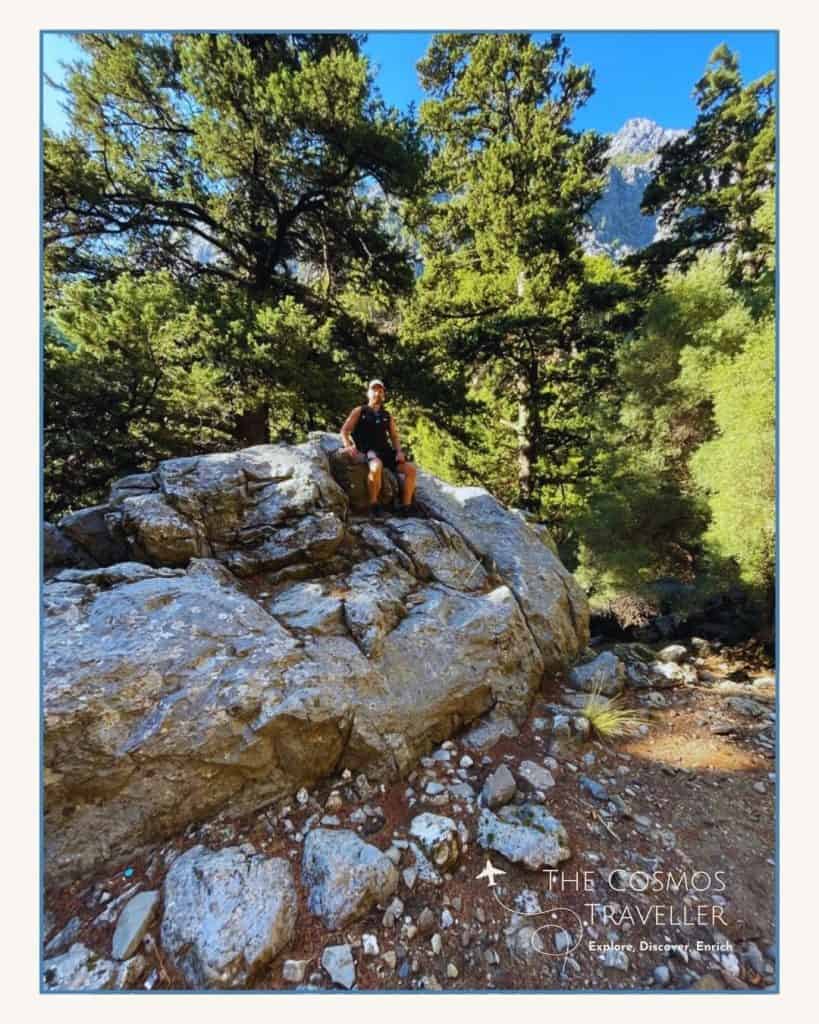 The Cosmos Traveller sitting on a rock in the forest section of the Samaria Gorge hike.