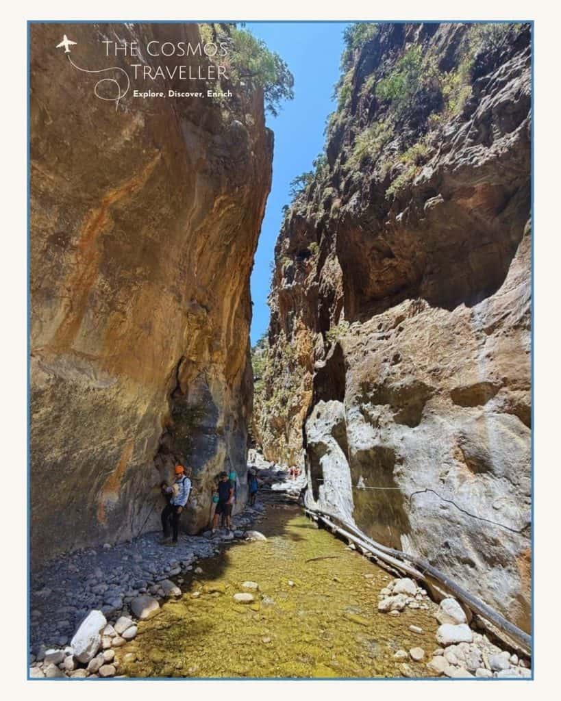 Hikers walking through the narrow Iron Gates of Samaria Gorge beneath towering cliffs.