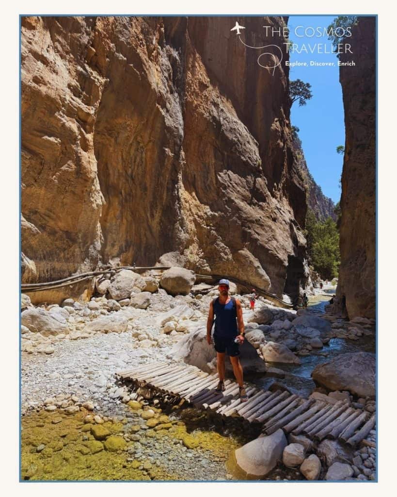 Man posing for photo on wooden bridge in a narrow section of the Samaria Gorge in Crete.