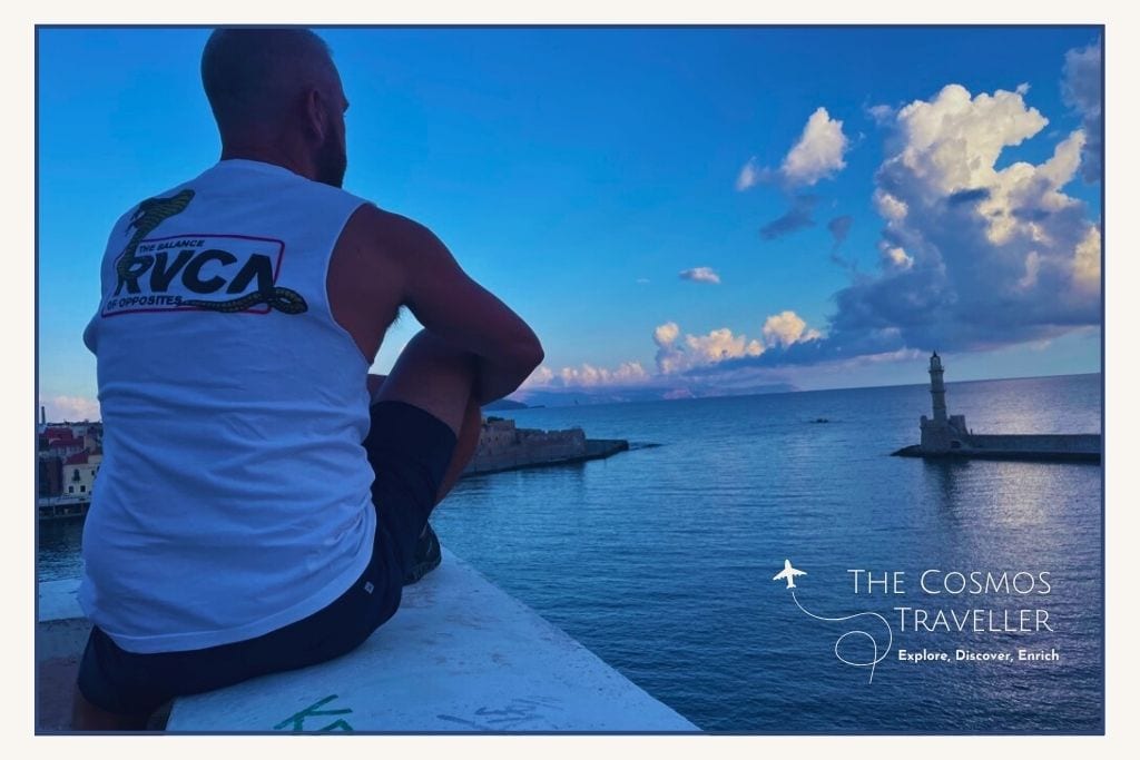 Person sitting on a wall overlooking Chania harbour with its iconic lighthouse and sea views below.