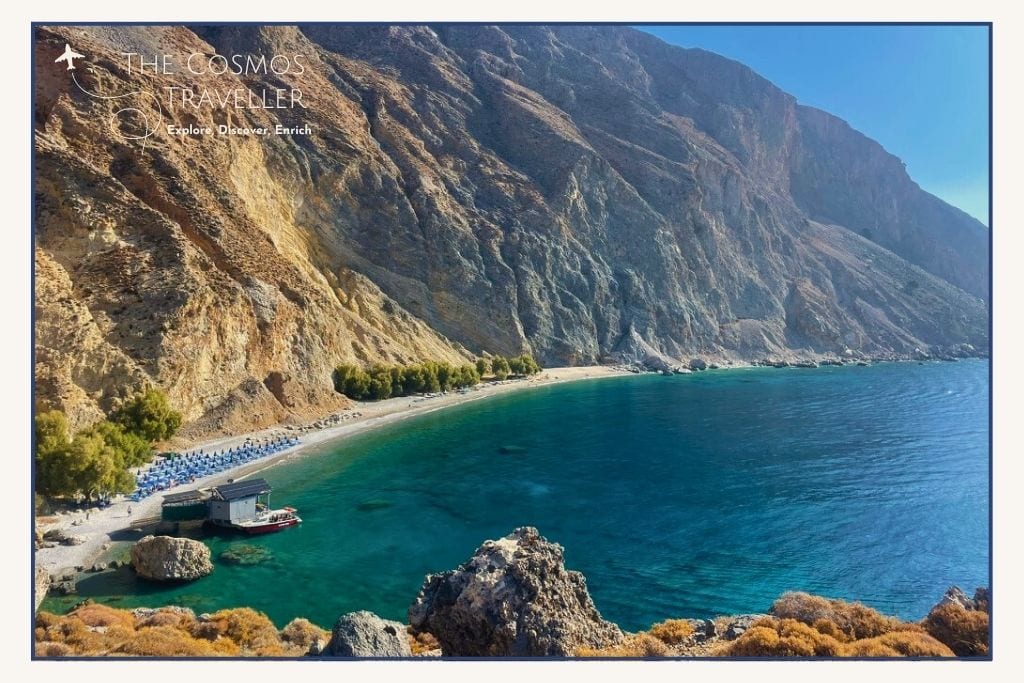 Dramatic cliffs behind Glyka Nera Beach, Crete, with tree-lined slopes and clear turquoise waters from above.
