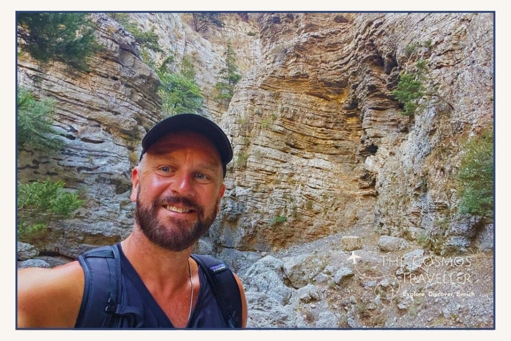 Hiker in Imbros Gorge, Crete, with steep narrow cliffs towering on both sides of the rocky trail.