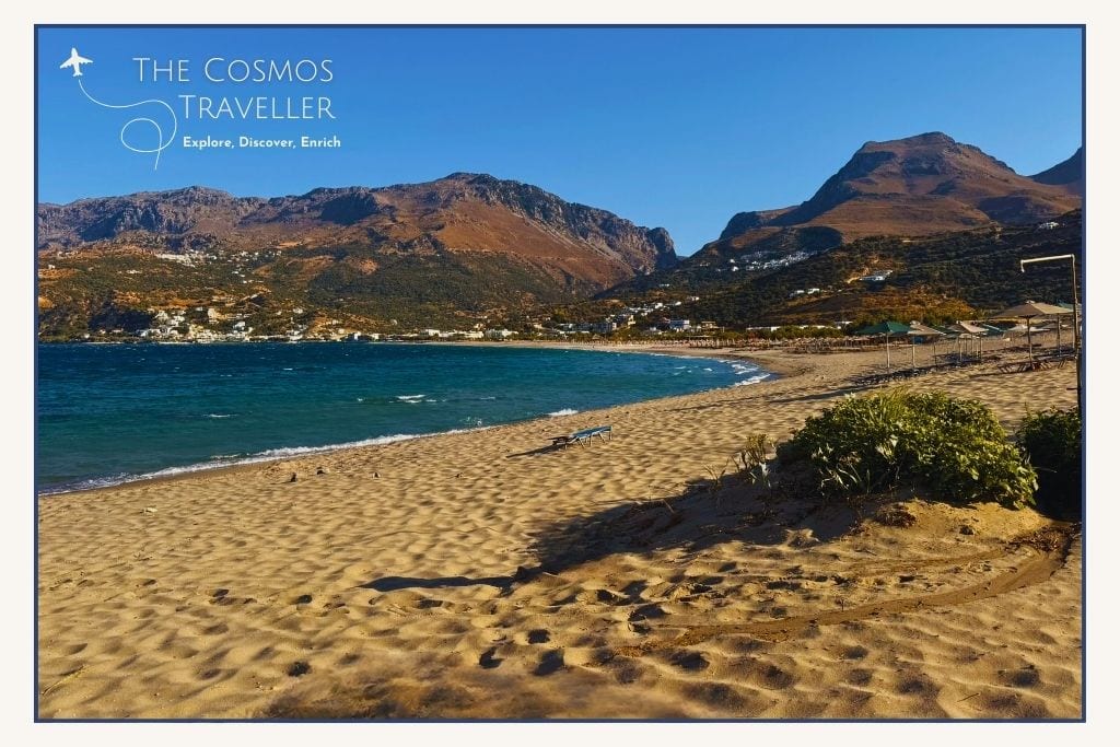 Photo of Paligremnos Beach, sandy shoreline beneath towering cliffs at the eastern end of Plakias Bay.