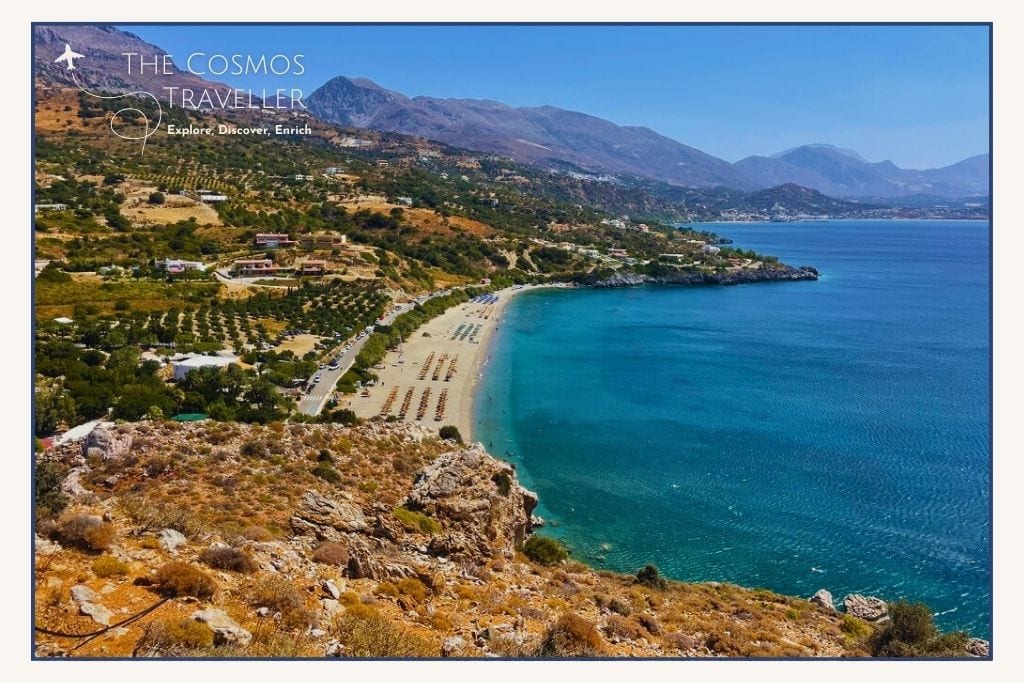 Photo of Souda Beach from the road above, showing sandy shoreline, organised sunbeds, and the Finikas valley backdrop.