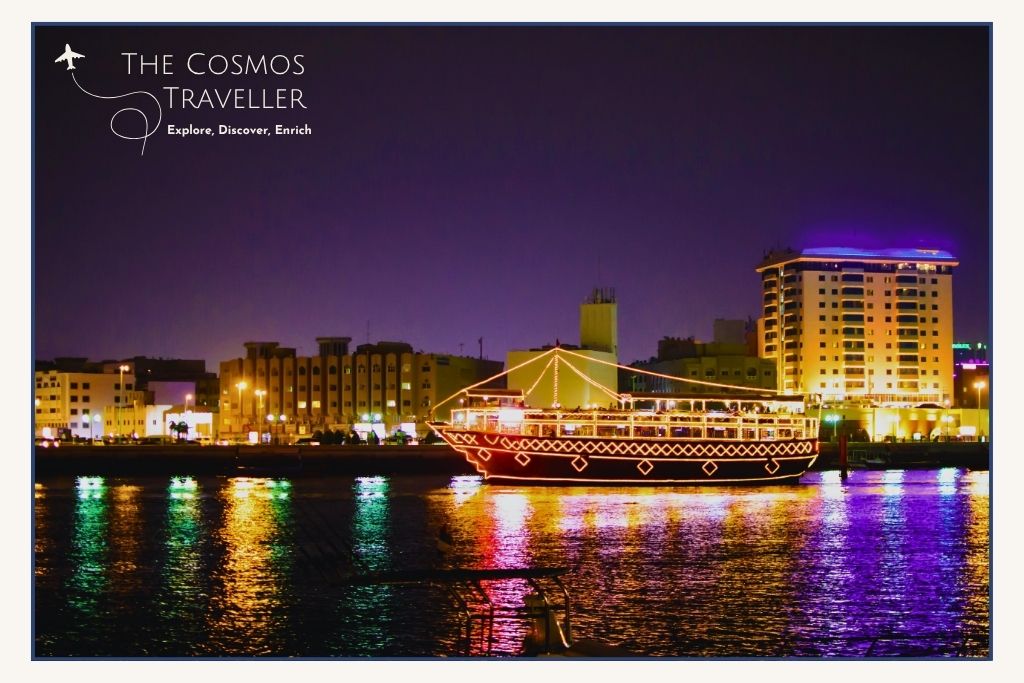 Traditional wooden dhow sailing along Dubai Creek with the city lights shimmering on the water.