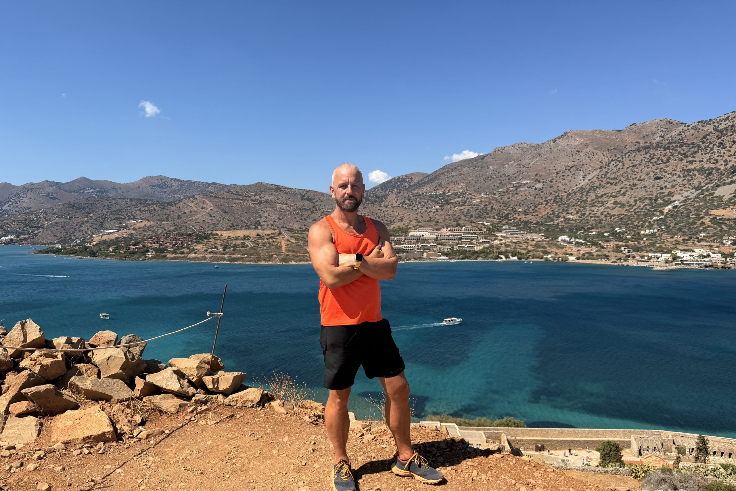 Rich, The Cosmos Traveller, standing on a rocky outcrop above the azure mediterranean waters.